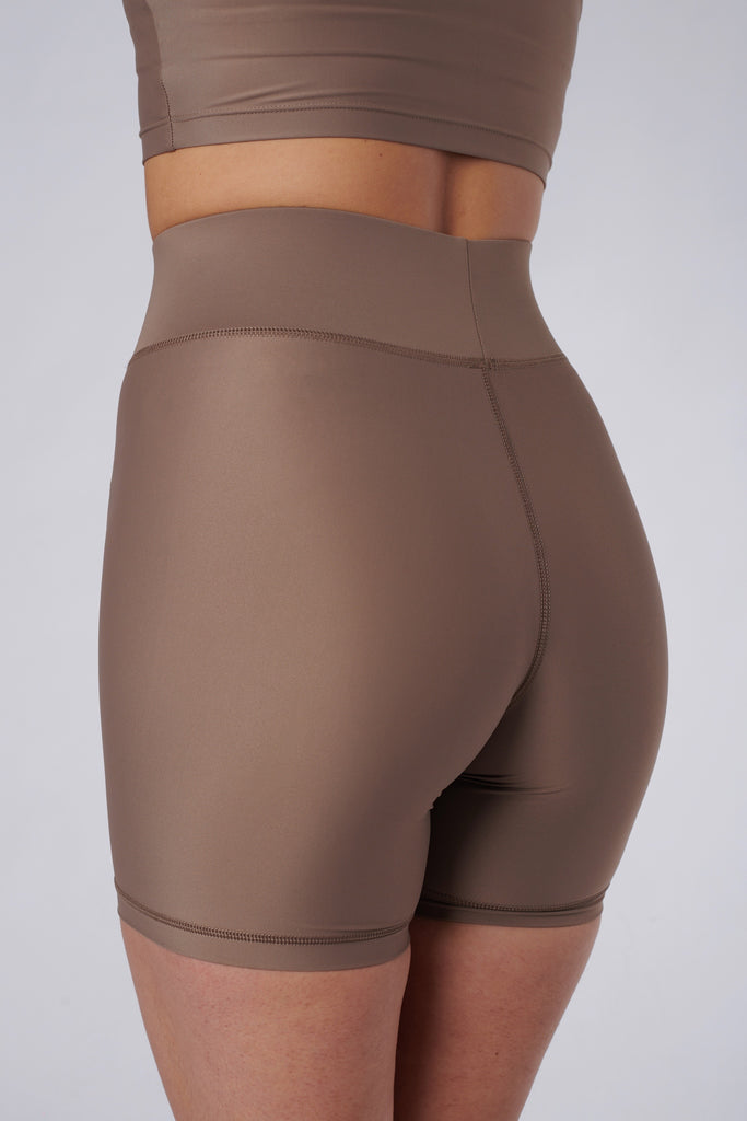 High-waisted beige bicycle shorts with a secure, compressive fit. No front seam and flattering wide waist band, close up